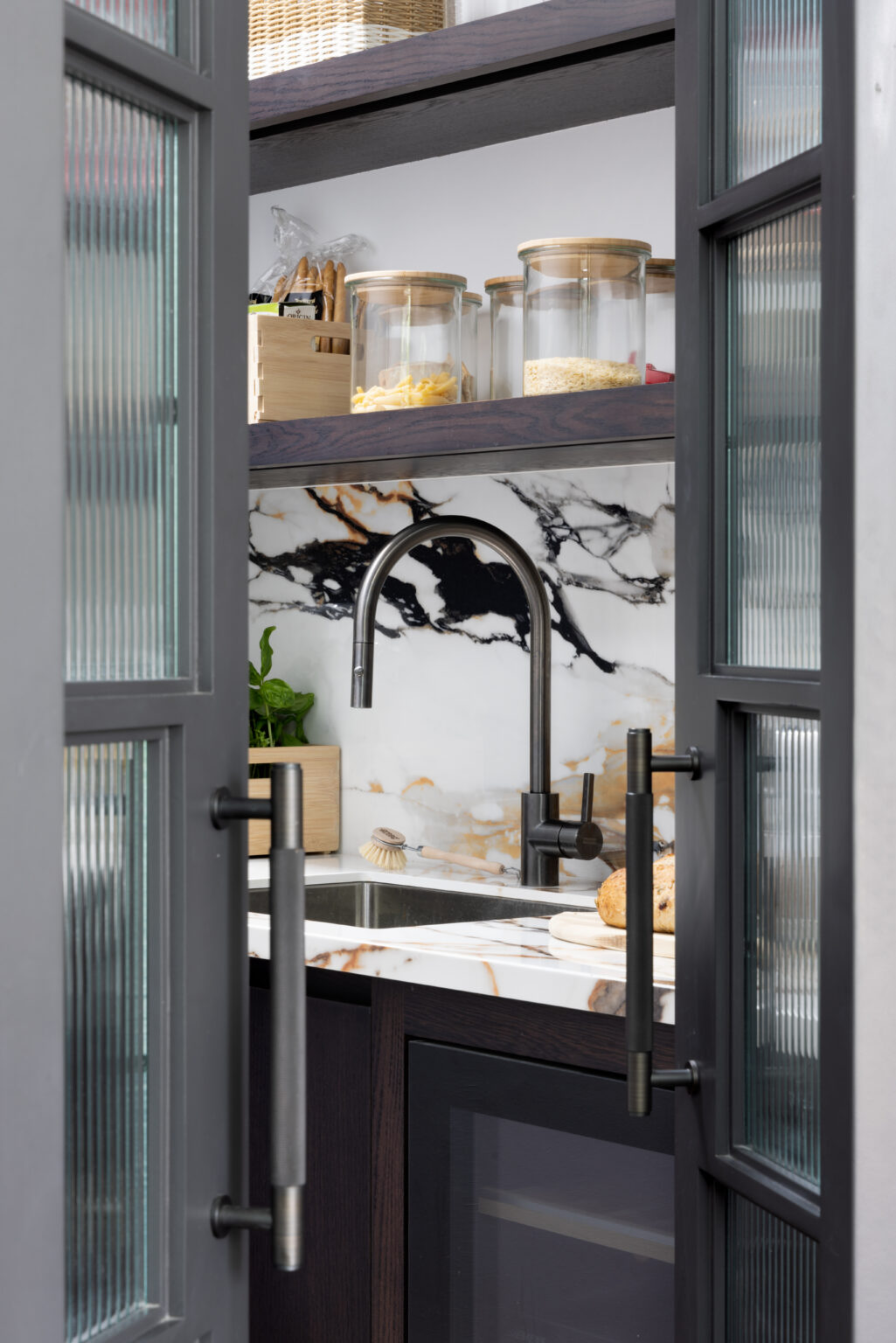 Glazed crittall doors open to reveal the walk-in pantry sink, tap and moving stone splashback beyond