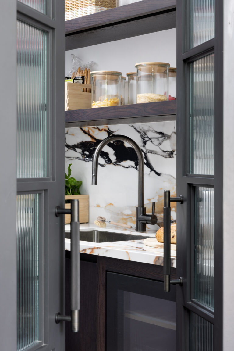 Glazed crittall doors open to reveal the walk-in pantry sink, tap and moving stone splashback beyond