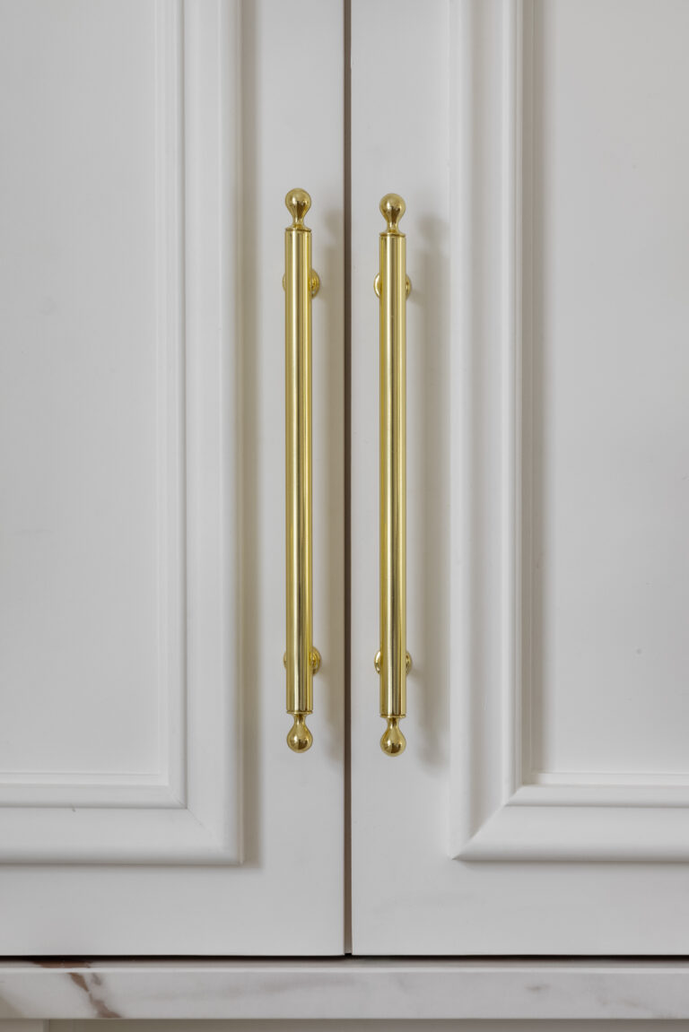 Close-up of panelled white cabinet doors fitted with elegant brass bar handles and matching end finials
