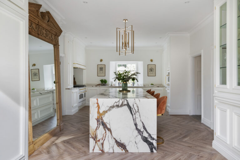 White kitchen with a gold-veined XTONE island, antique mirror, burnt-orange velvet stools and herringbone wood flooring