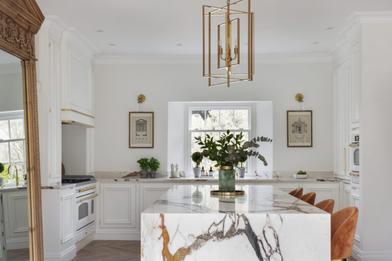 White kitchen with gold-veined XTONE island, brass fittings, burnt-orange velvet stools and an antique mirror
