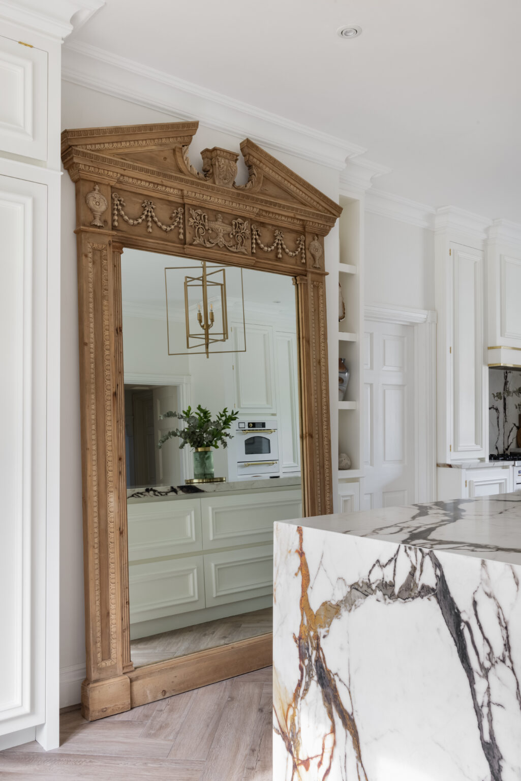 Antique carved wood mirror beside an XTONE island with deep golden veining in a white kitchen