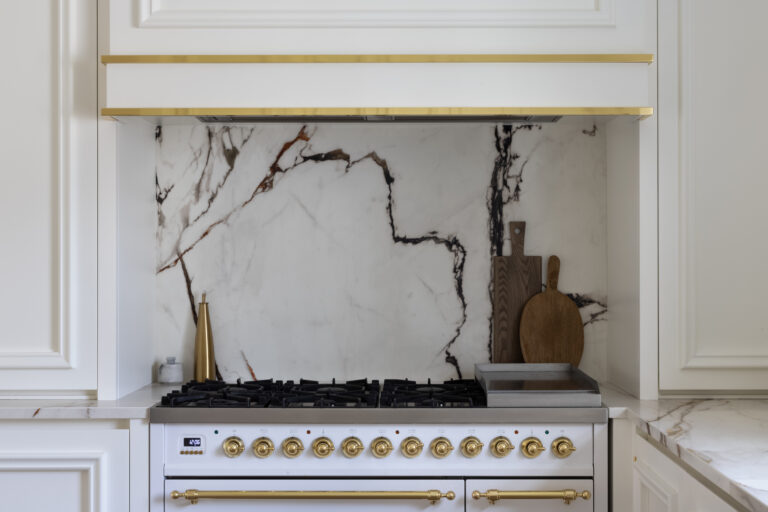 White range cooker with brass knobs beneath a veined stone splashback and extractor with brass trim