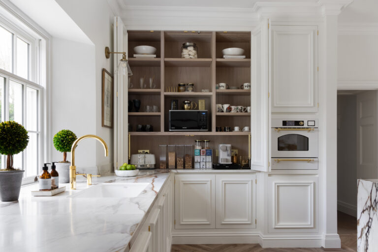 White kitchen with brass taps, veined worktop, built-in oven and an open shelving pantry cupboard