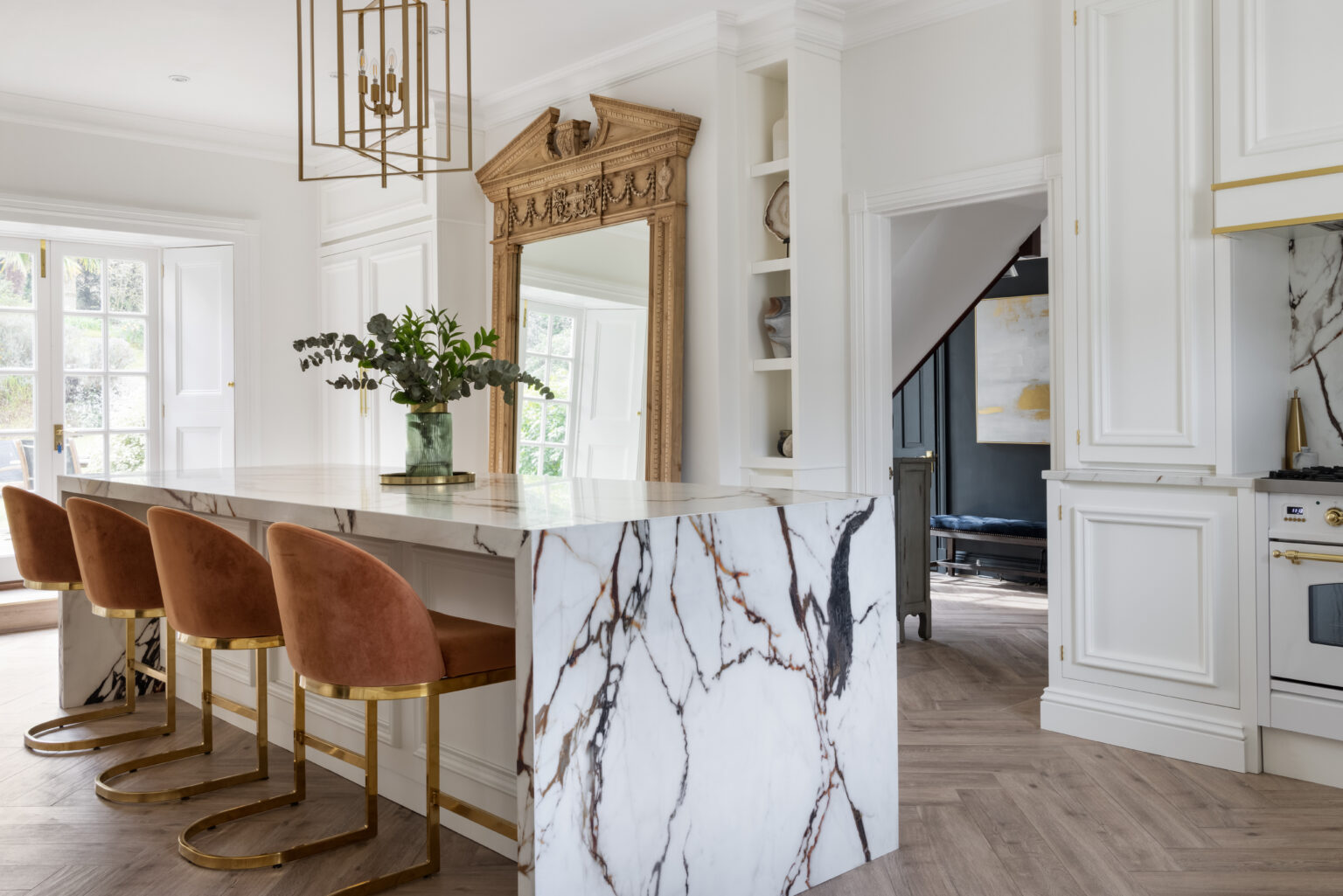 Kitchen island with veined XTONE top, burnt-orange velvet stools and an antique-style gilt mirror beyond
