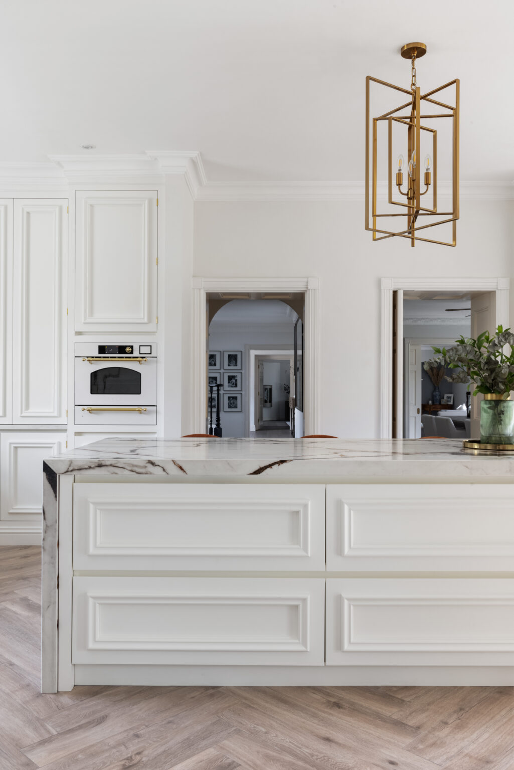 White kitchen island with gold-veined XTONE worktop, brass pendant light and panelled cabinetry below