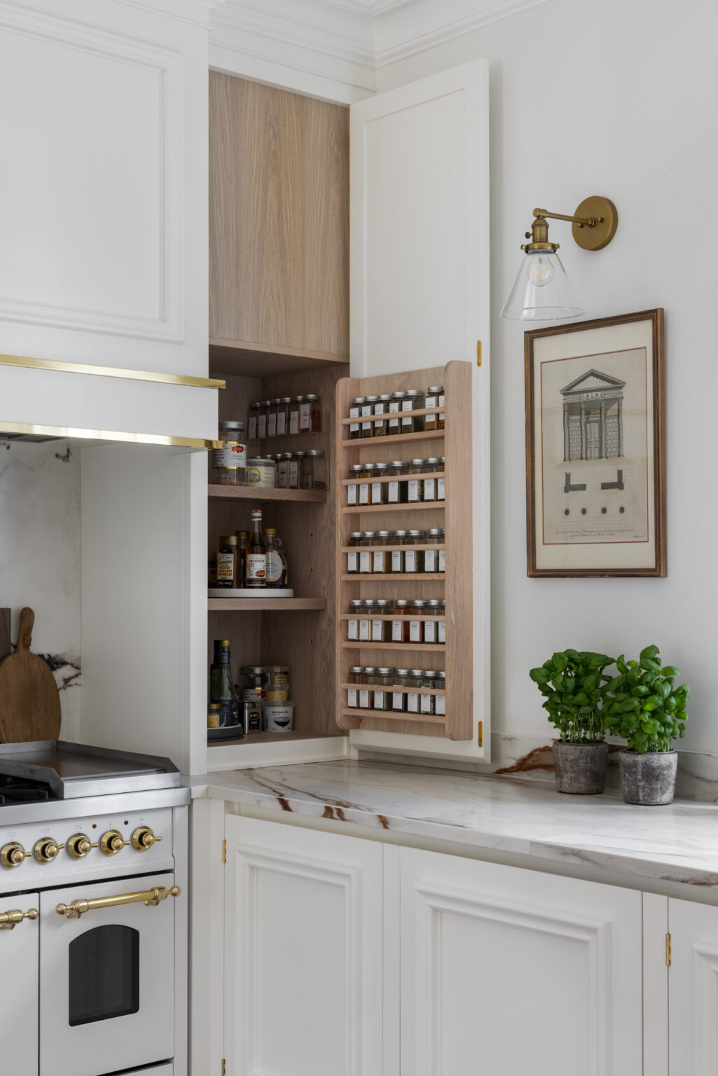 White cabinetry with an open pantry door revealing a built-in spice rack, shelves, brass range cooker and stone worktop