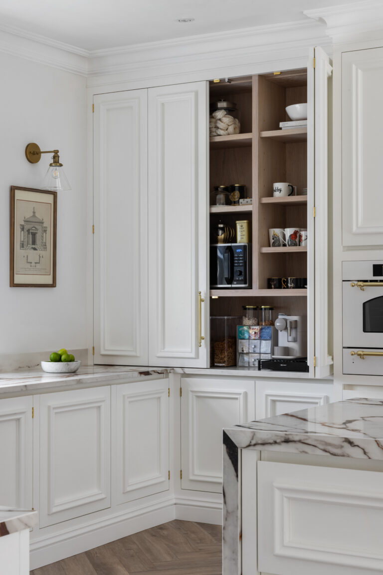 White panelled kitchen cabinetry with a concealed pantry cupboard revealing shelves, mugs, microwave and coffee machine