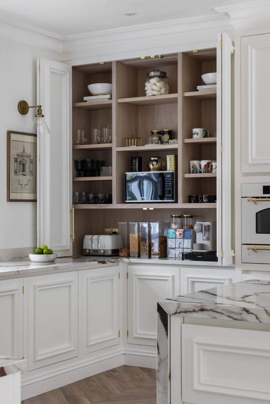 White pantry cupboards open to reveal shelves with crockery, jars and small appliances beside the veined XTONE island