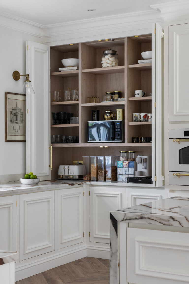 White pantry cupboards open to reveal shelves with crockery, jars and small appliances beside the veined XTONE island