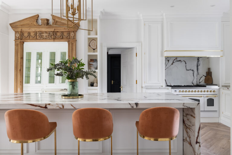 White kitchen with antique mirror, XTONE island with golden veins, burnt-orange velvet stools and brass fittings