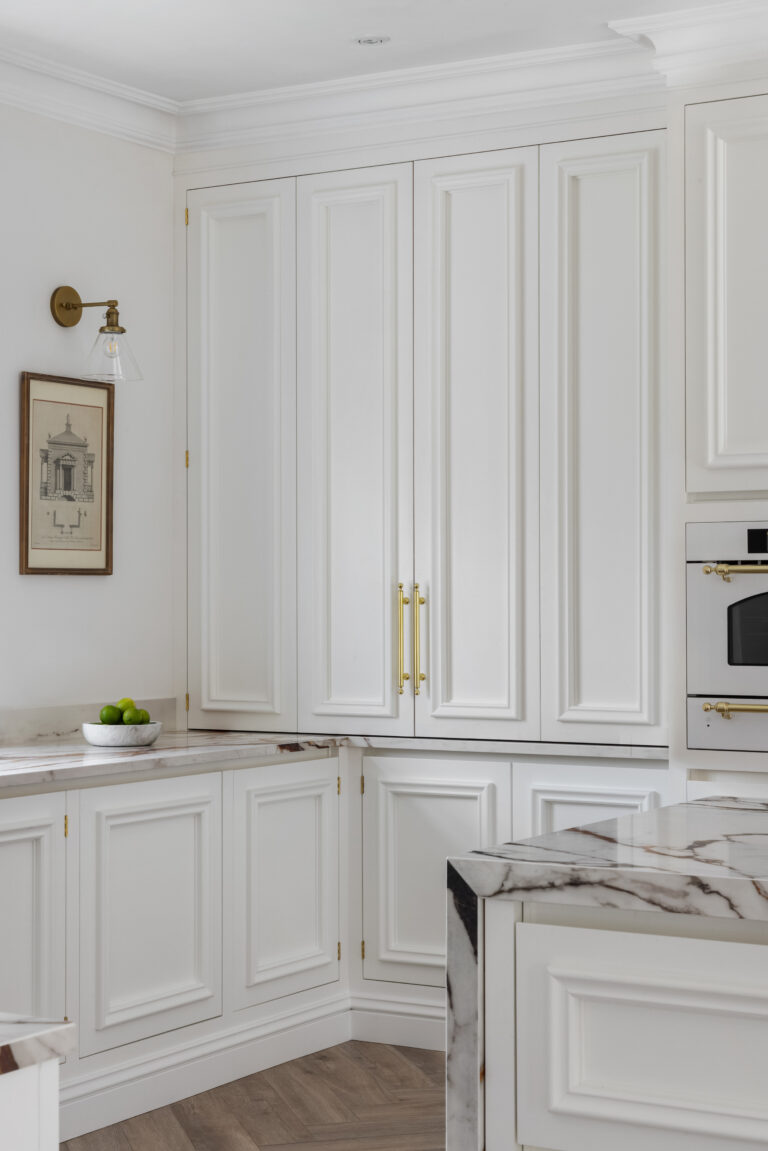 White panelled kitchen cabinetry with brass handles, an XTONE island and integrated oven with brass trim