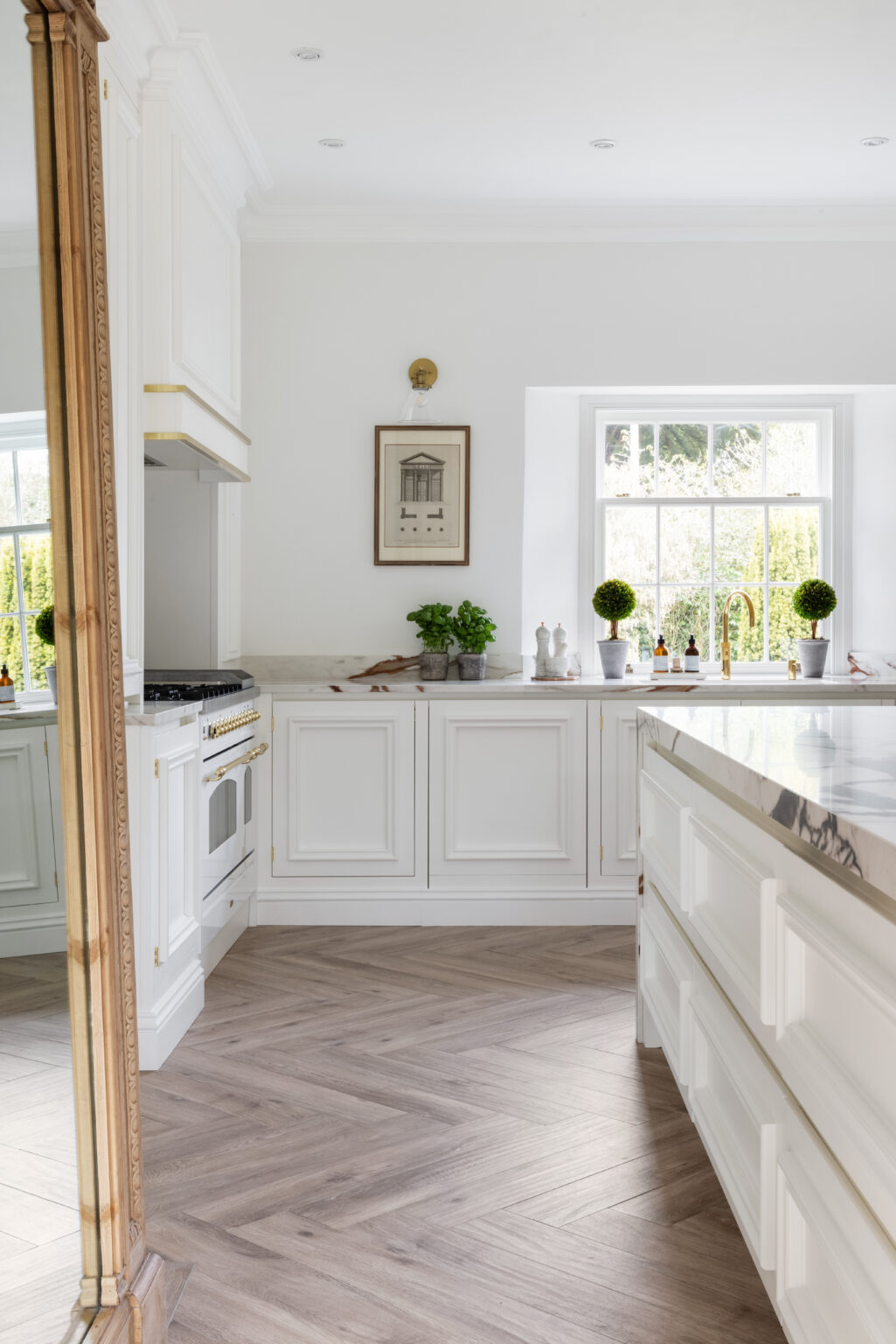 White kitchen with antique mirror, XTONE island, brass fittings and herringbone flooring by the window
