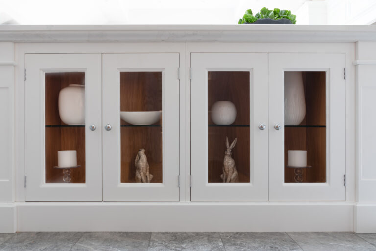Glass-fronted cupboard doors display ceramic vases, bowls and hare figurines against a timber-lined interior