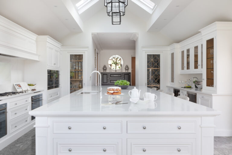 White kitchen with a long island, Silestone worktop, vaulted ceiling and matching pantry and wine store niches either side