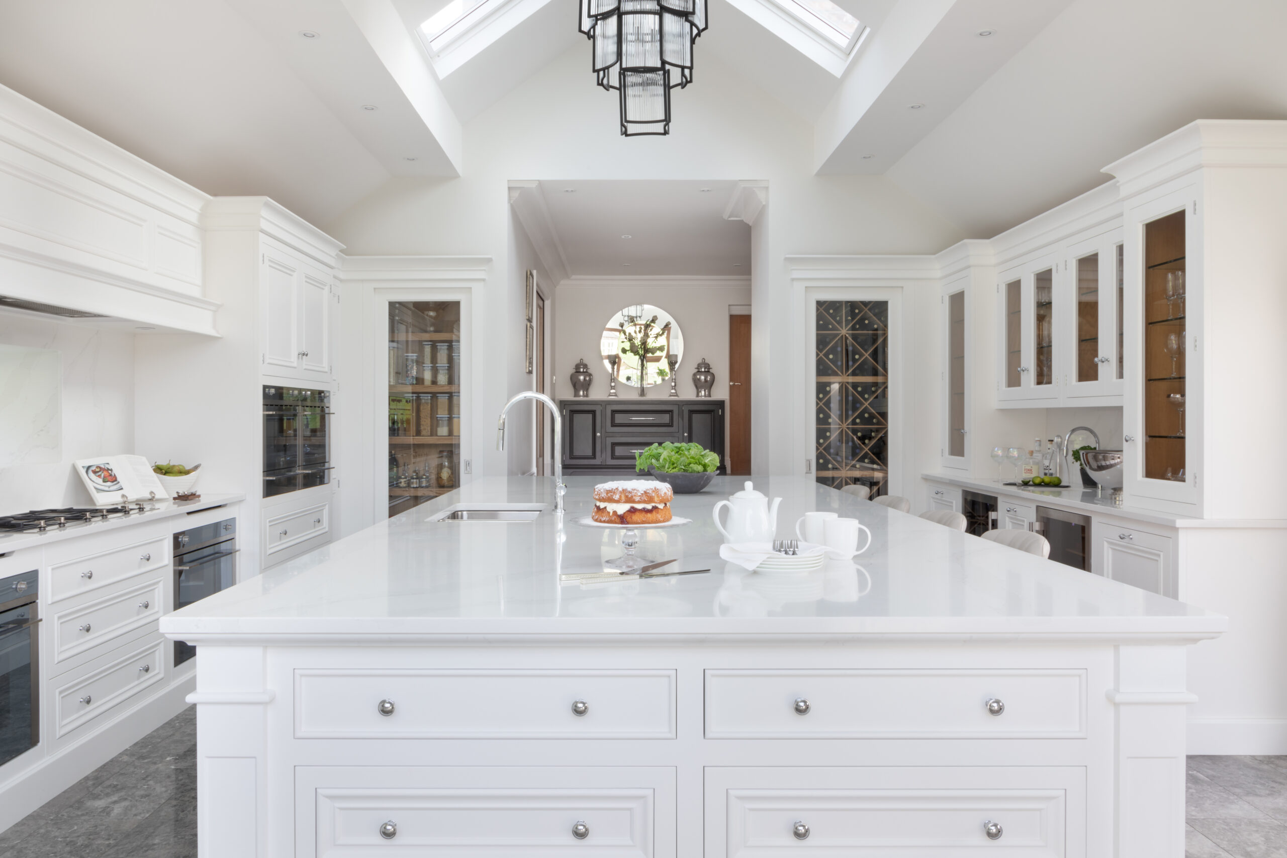 White kitchen with a long island, Silestone worktop, vaulted ceiling and matching pantry and wine store niches either side
