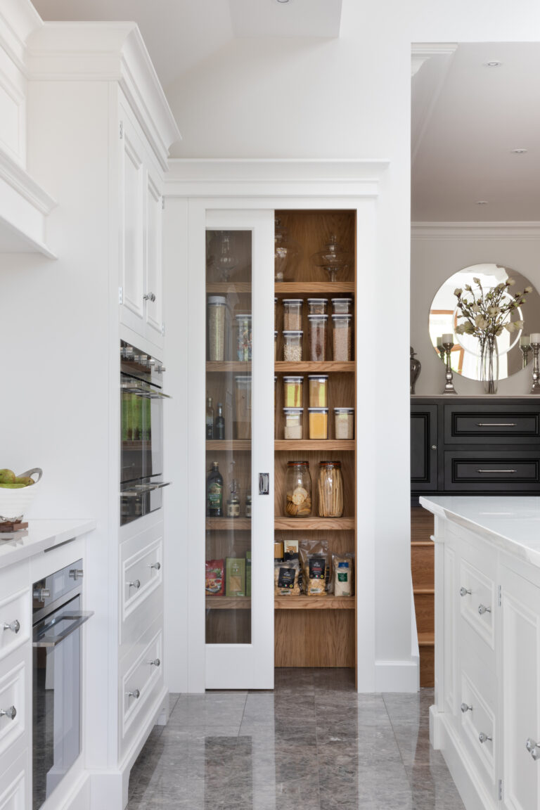 Walk-in pantry niche with glazed sliding door, timber shelving and stacked storage jars beside white cabinetry