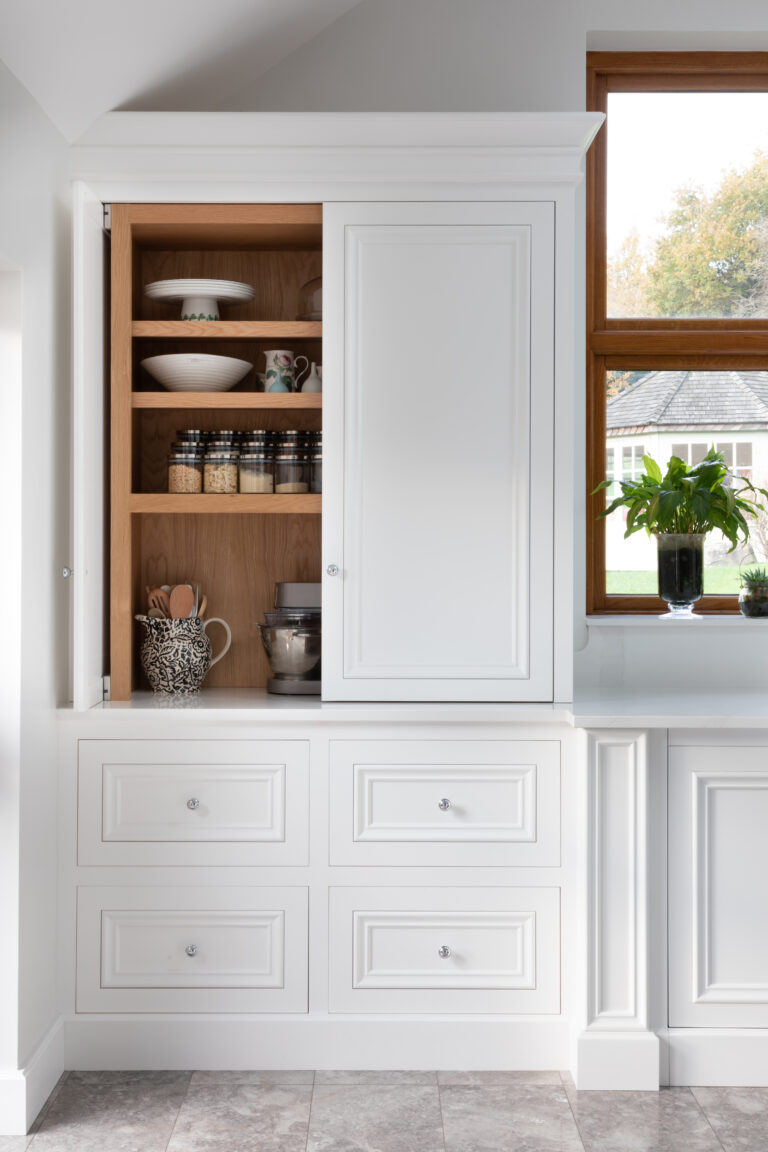 Built-in walk-in pantry niche with open shelving, crockery and jars, set beside drawers and a window