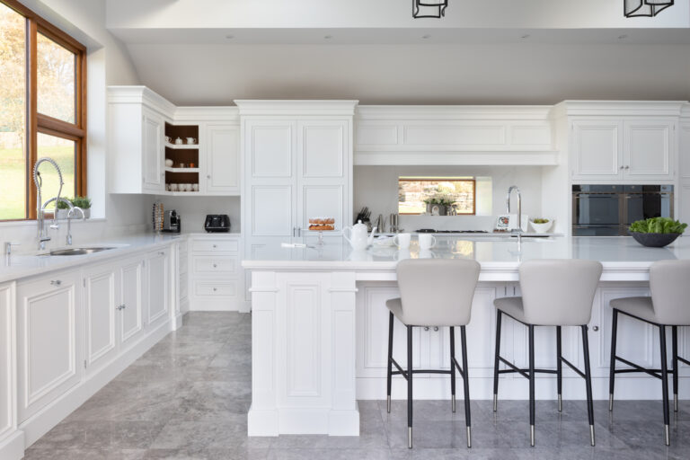 Large white kitchen with Silestone worktops, a long island, bar stools and panelled cabinetry beneath a vaulted ceiling