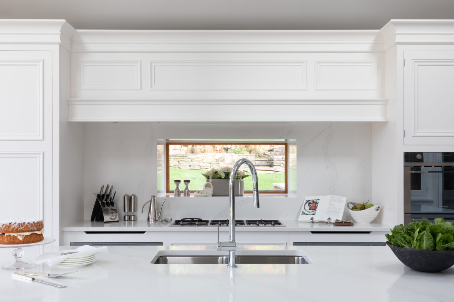 White kitchen island with sink and tap, Silestone worktops, hob and window overlooking the garden beyond