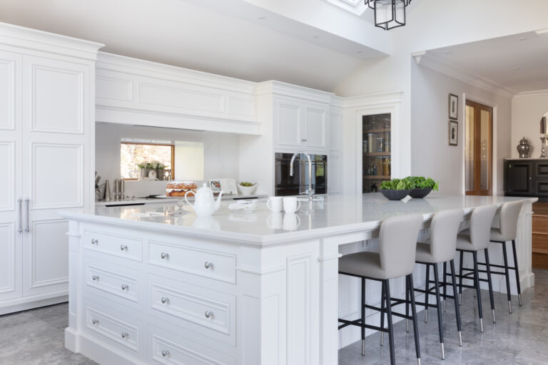Large white kitchen island with Silestone worktop, built-in drawers and bar stools beneath a vaulted ceiling