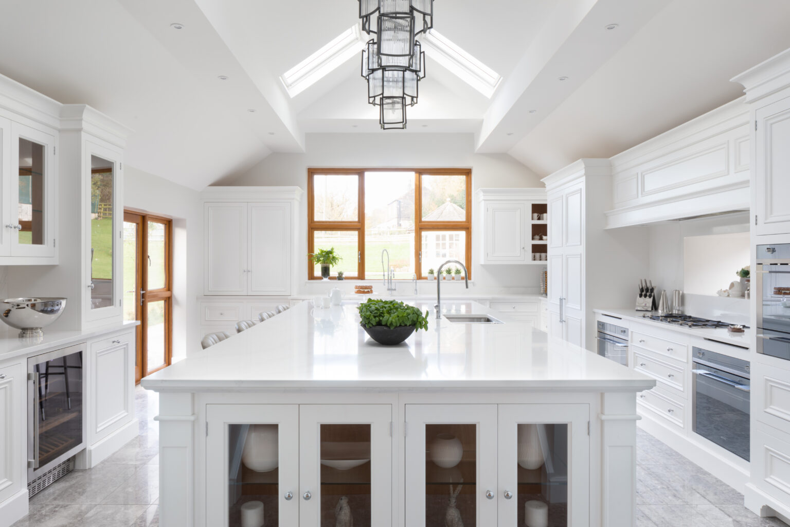 Large white kitchen with a long island, Silestone worktops, glazed display cabinets and a vaulted, skylighted ceiling