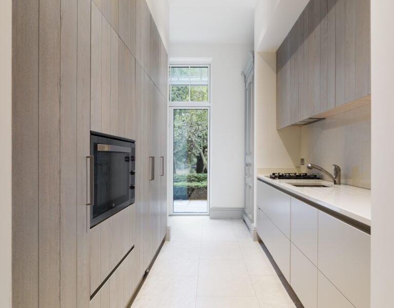 Galley kitchen with tall timber cabinetry, built-in oven, and fitted hob and sink beside a garden door