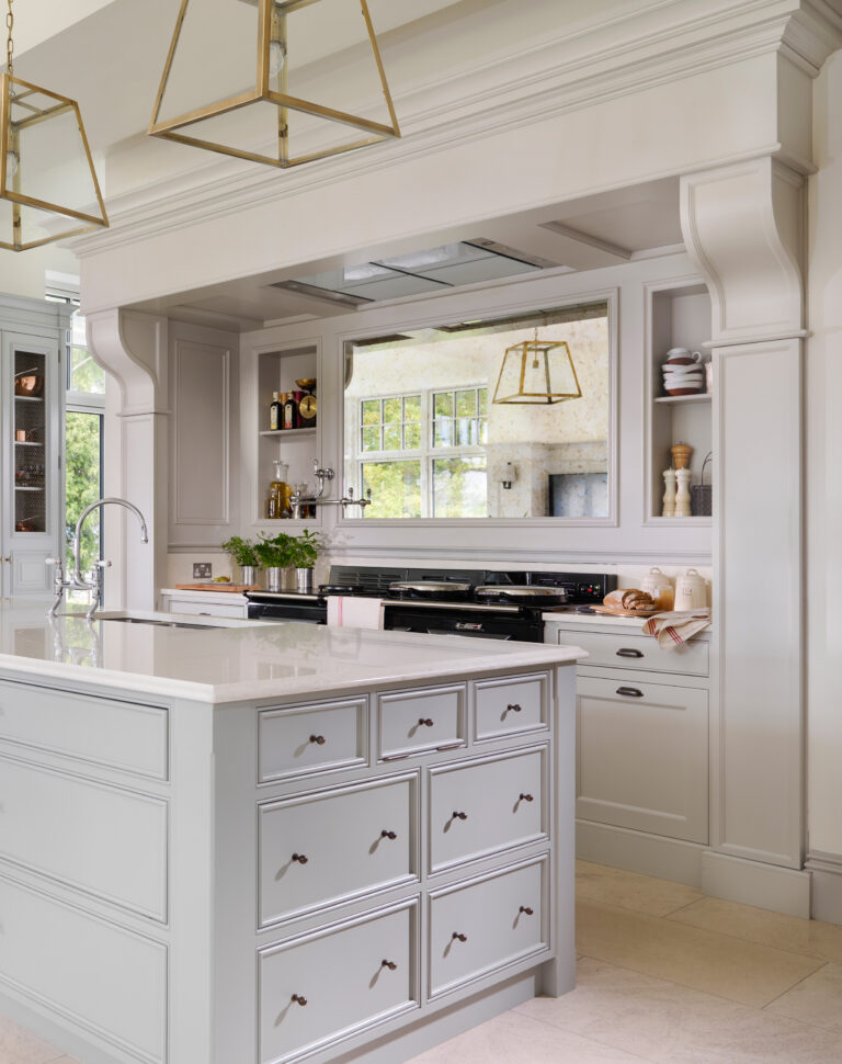 Bespoke overmantel frames a black Aga and mirrored backsplash above a pale grey island with brass pendant lights
