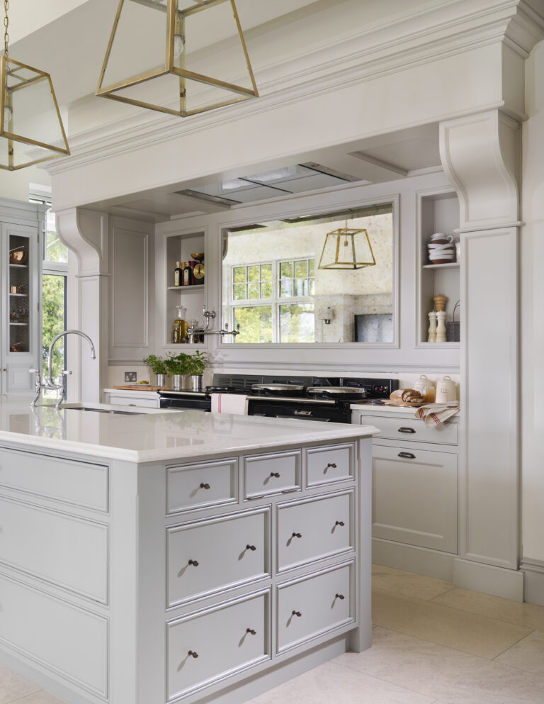 Bespoke overmantel frames the Aga, with mirrored backsplash, brass pendant lights and a large island with brass handles