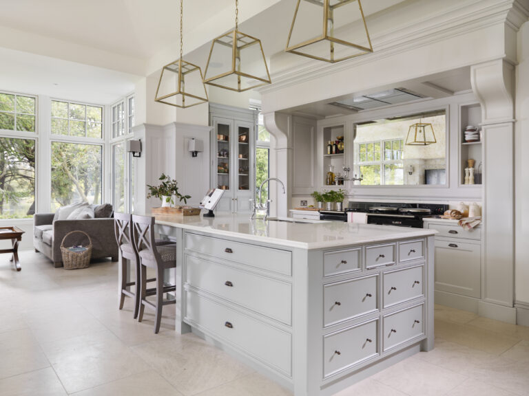 Large kitchen island with pale cabinetry, brass lantern pendants, and an Aga beneath a mirrored overmantel backsplash