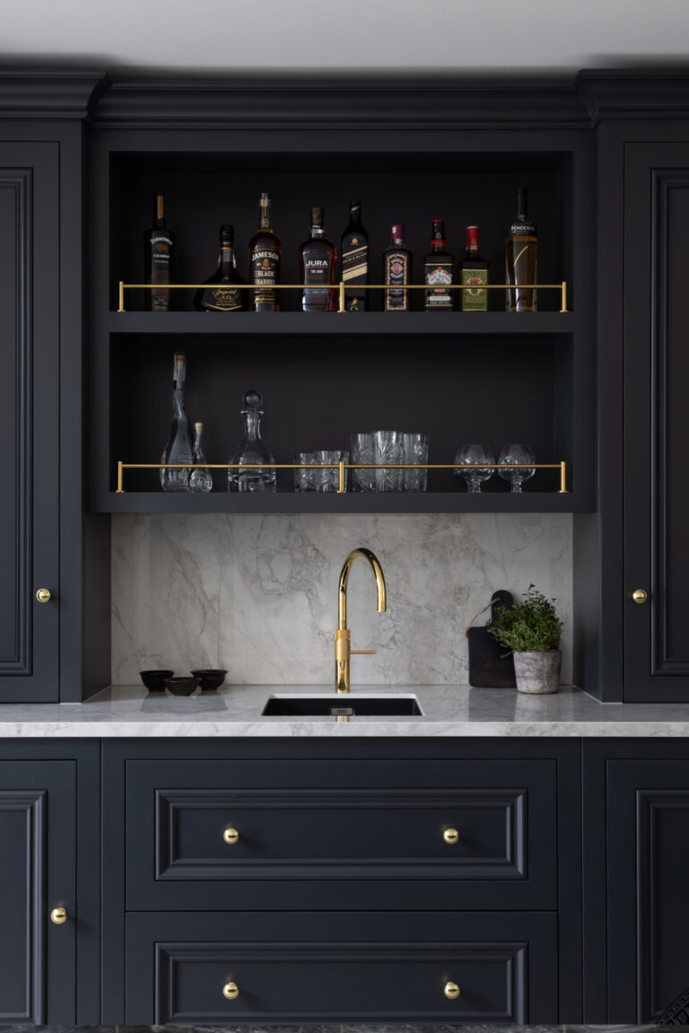 Built-in bar nook with dark cabinetry, open shelving for spirits and glassware, brass tap and stone splashback
