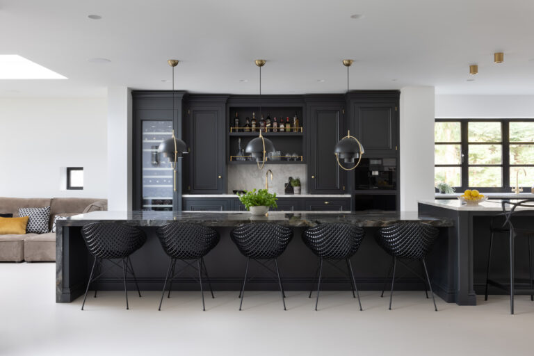 Dark kitchen island with XTONE Orobico Dark stone top, woven bar stools and brass pendant lights over a wine fridge and drinks shelf