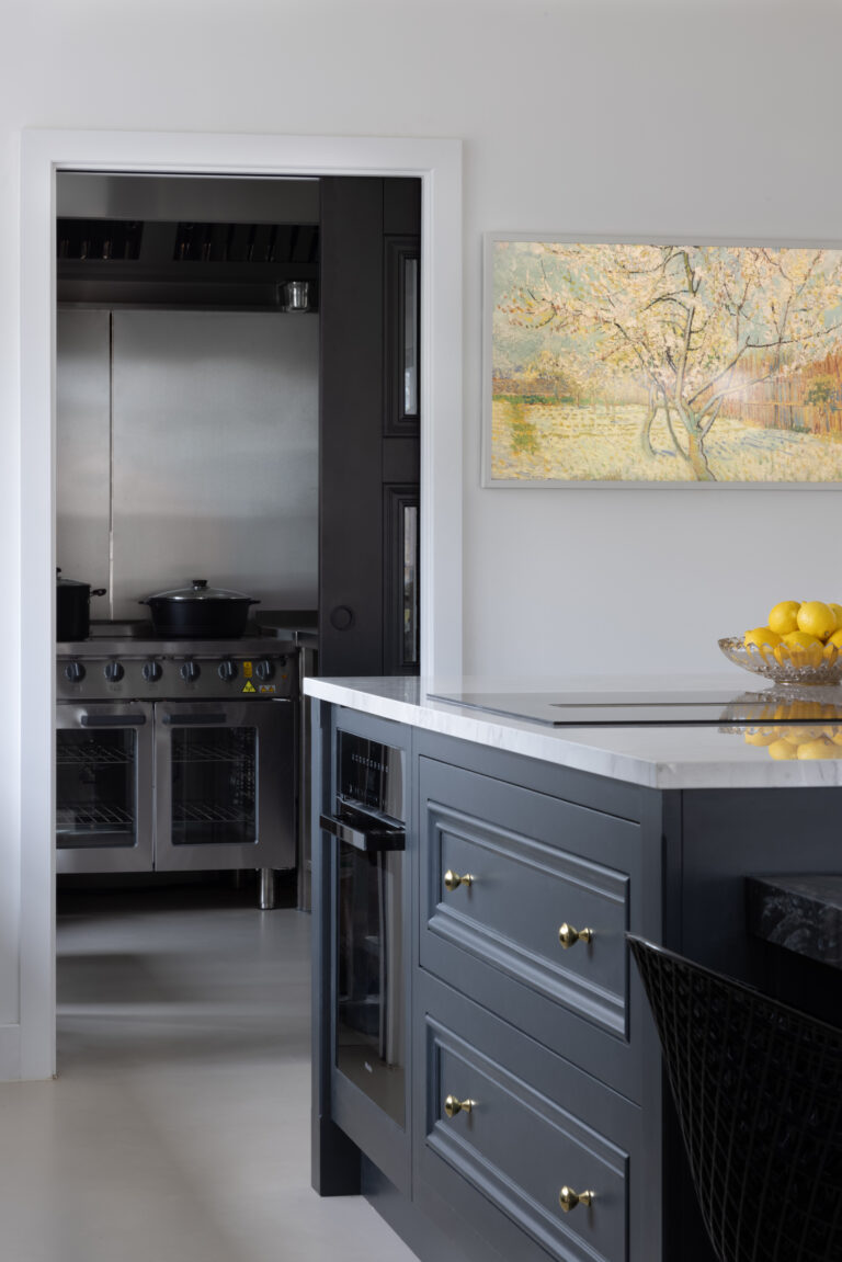 Kitchen island with brass handles beside a doorway leading to a hidden prep kitchen with stainless steel ovens