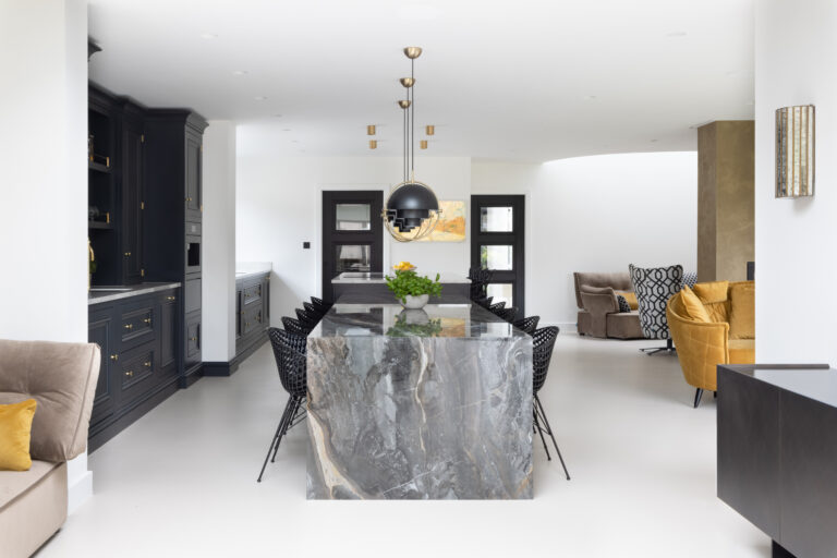 Open-plan kitchen with an XTONE Orobico Dark stone island, dark cabinetry, wire chairs and poured resin flooring beyond