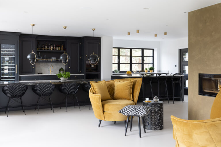 Dark kitchen island with XTONE Orobico Dark stone top, black bar stools, and mustard velvet armchair on poured resin flooring