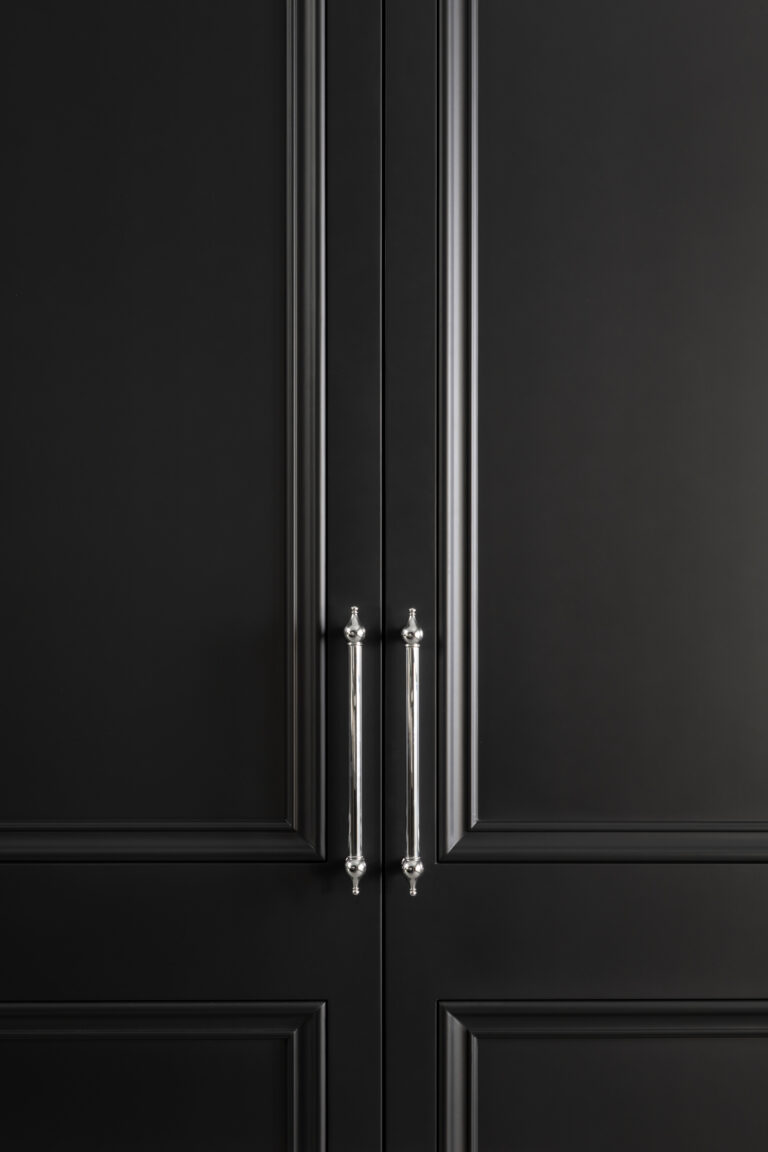 Close-up of black panelled cabinet doors with slender polished chrome bar handles and decorative finials