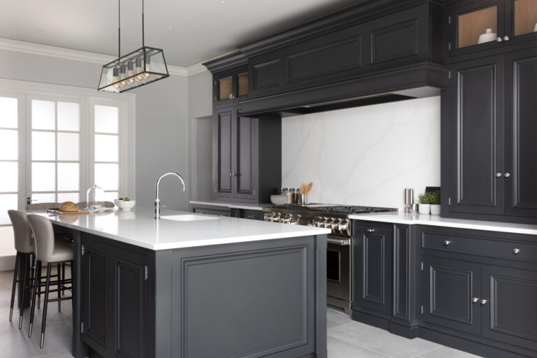 Black cabinetry surrounds a central island with white stone worktops, a sink and a range cooker beyond