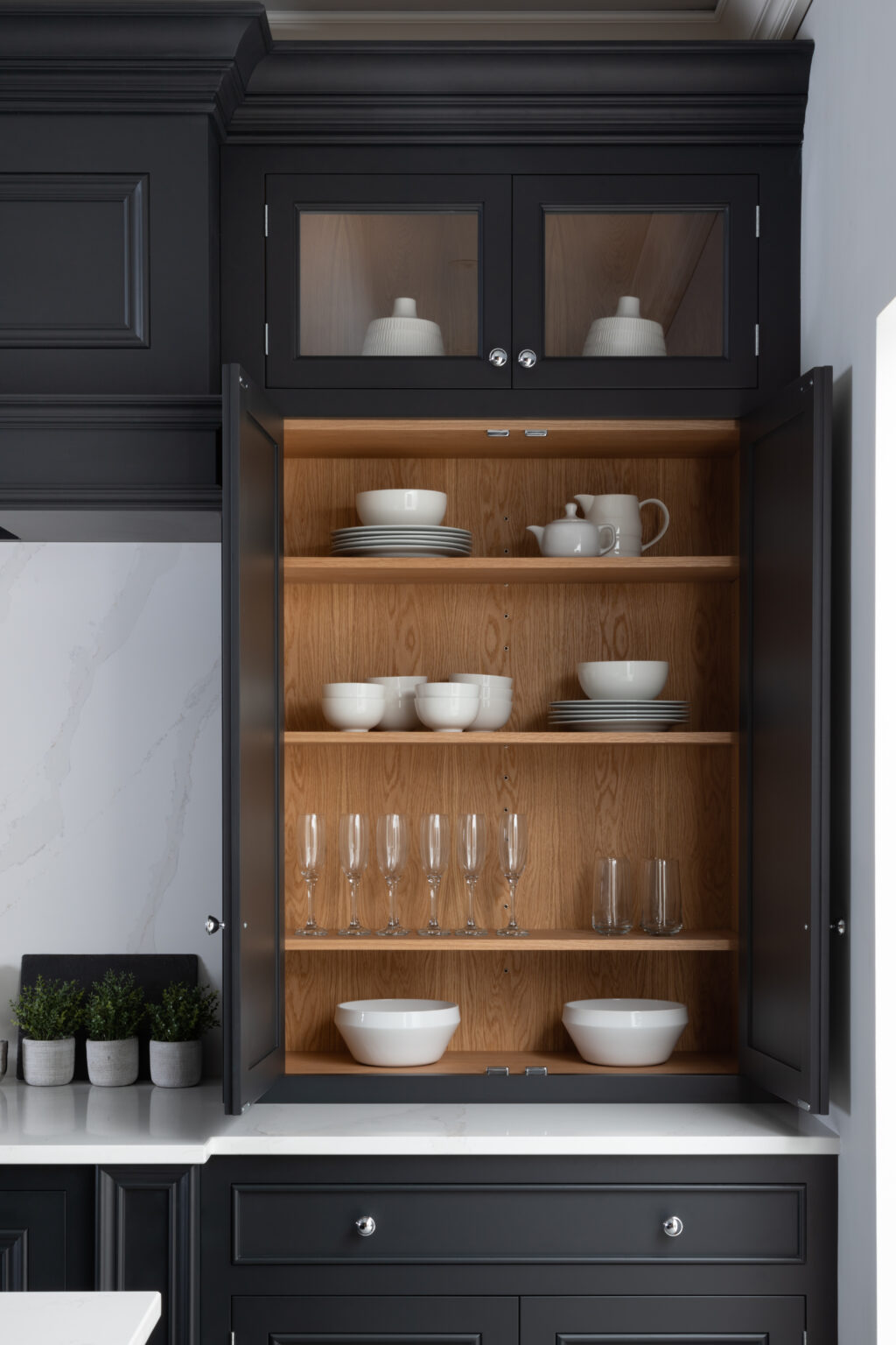 Tall dark glazed dresser with open shelves displaying white crockery, glassware and jugs against a white stone worktop
