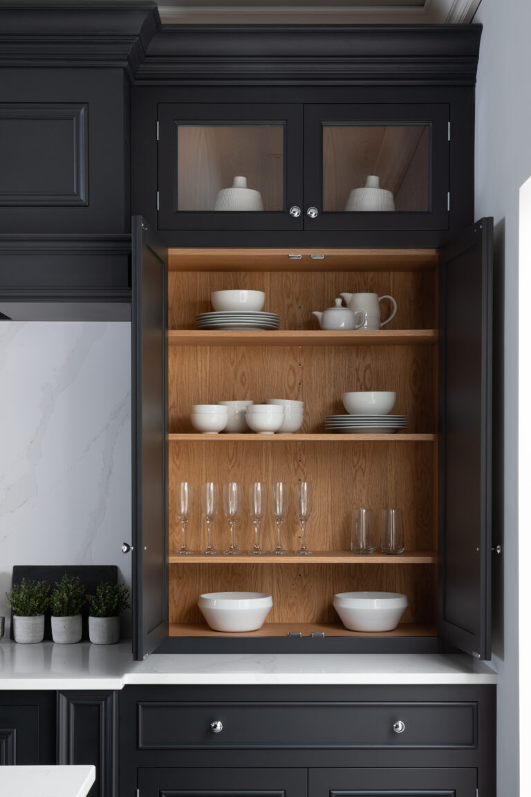 Tall dark glazed dresser with open shelves displaying white crockery, glassware and jugs against a white stone worktop
