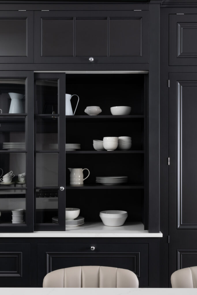 Tall black glazed dresser with sliding doors displaying white crockery, jugs and bowls on open shelves