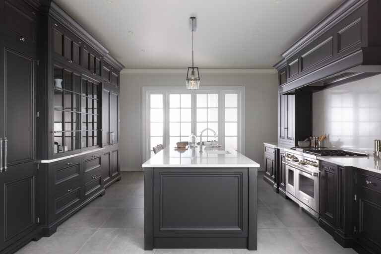 Dark cabinetry lines a kitchen with a central island, white stone worktops and a glazed dresser display