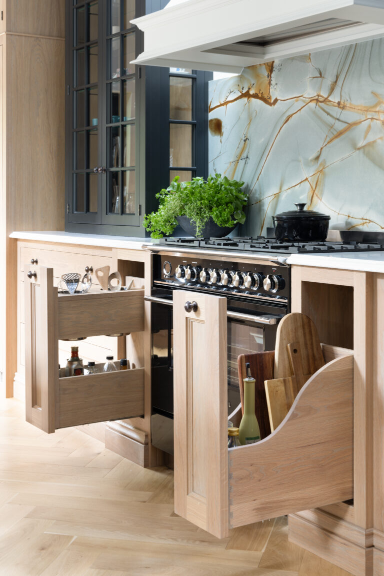Range cooker flanked by open custom pull-outs holding bottles and chopping boards, with backlit stone splashback behind