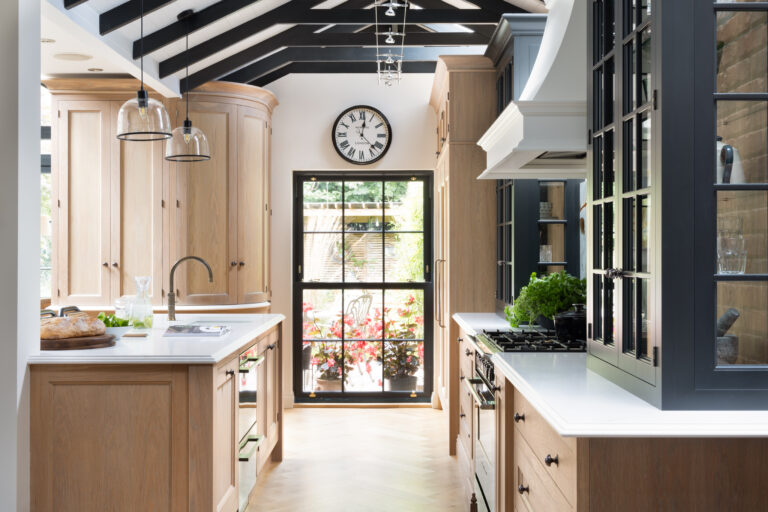 Kitchen with vaulted beamed ceiling, timber cabinetry, antique brass handles and a central island beneath glass pendant lights