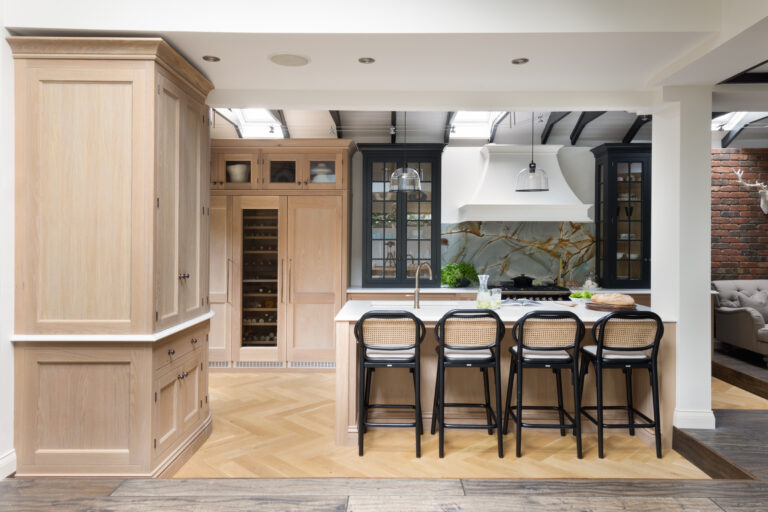 Open-plan kitchen with pale timber cabinetry, backlit stone splashback, white canopy and an island with cane bar stools