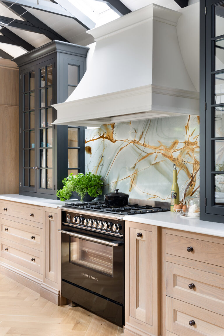Kitchen range cooker beneath a white canopy hood, with a backlit stone splashback and glazed display cabinets alongside