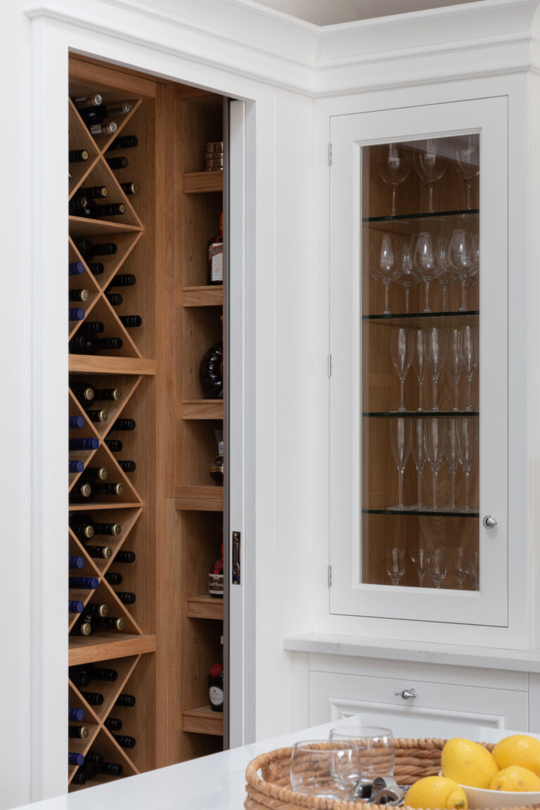 Open wine cabinet with diamond-shaped timber racking beside a glazed white cupboard displaying wine and champagne glasses