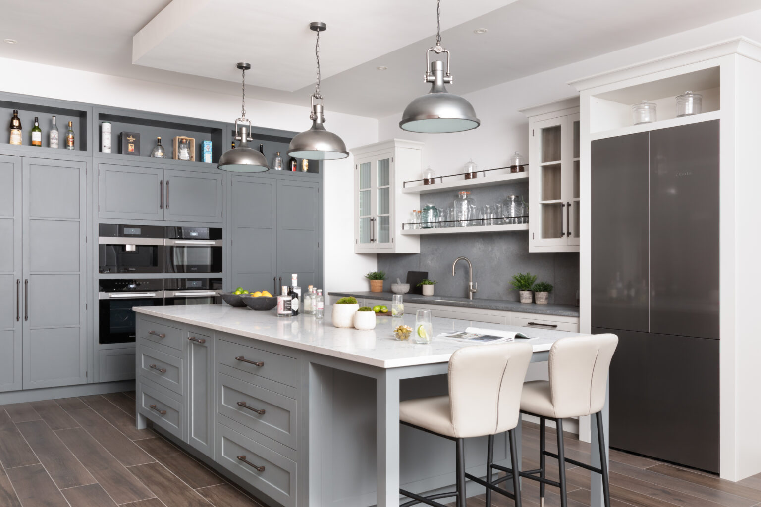 Kitchen island with bronze handles, stainless steel pendant lights, and built-in Miele appliances beside open shelving