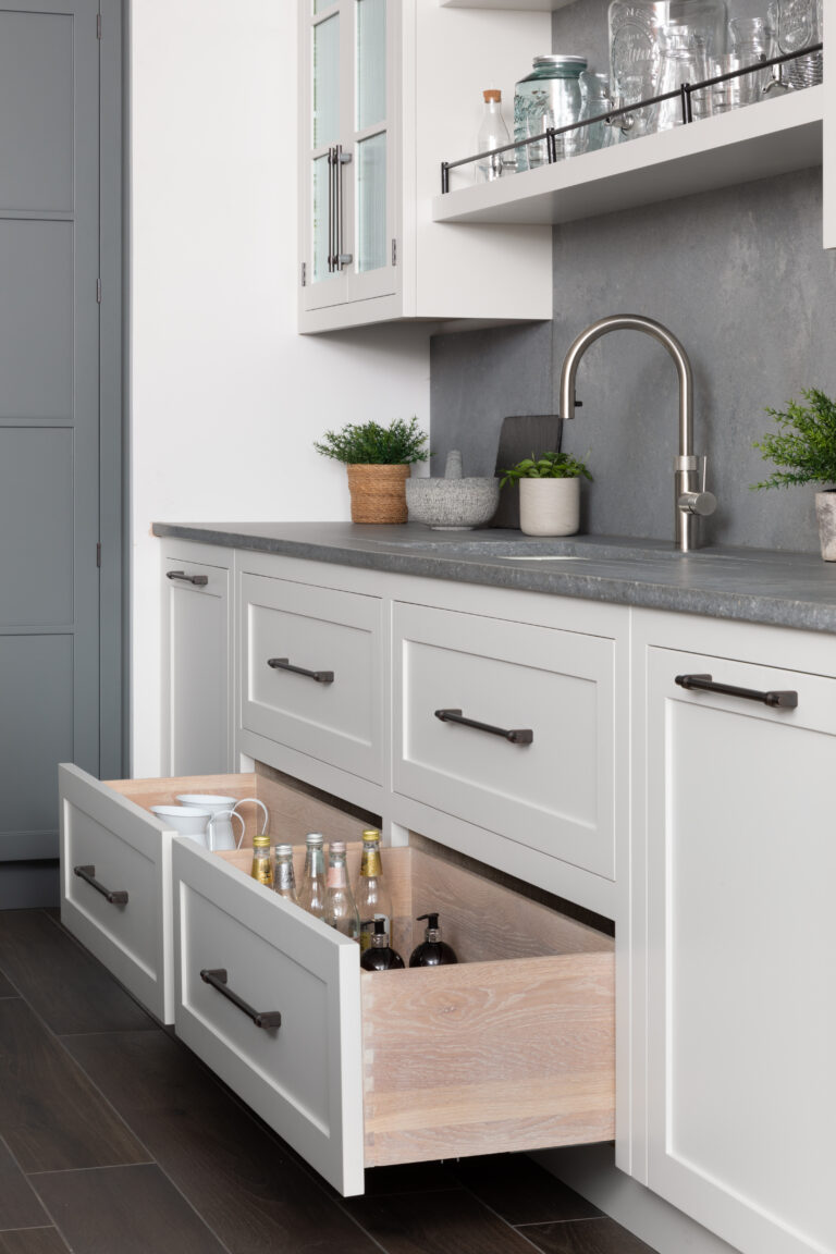 Bespoke cabinetry with bronze handles, open drawers, a stainless steel tap and sink, and glass storage jars on a shelf