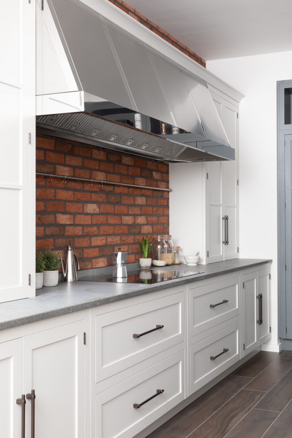 Stainless steel extractor hood above an exposed brick splashback, with bronze-handled cabinetry and induction hob