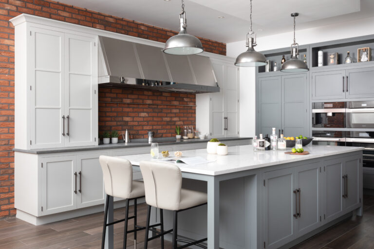 Kitchen island with bronze handles, bar stools and pendant lights, exposed brick wall and stainless steel extractor hood